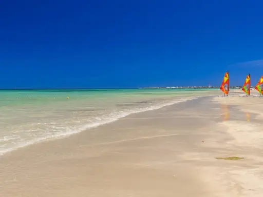 Piękna plaża w Tunezji, idealna na kwiecień. Trzy kolorowe deski windsurfingowe czekają na wiatr.