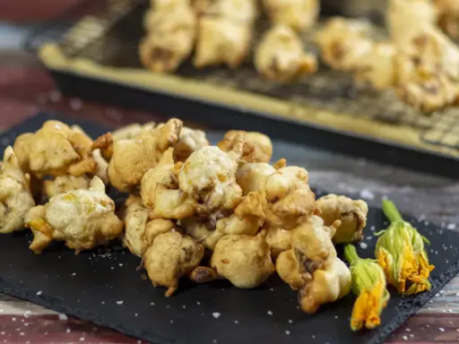 Frittelle di fiori di zucca dorate e croccanti, servite su una lavagna con fiori freschi e sale grosso.