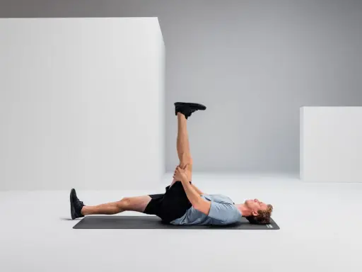 Mann liegt auf Matte, dehnt Bein für Hamstring Training.