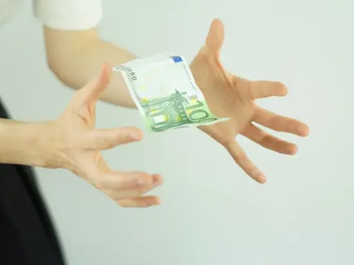 Hände fangen einen 100-Euro-Schein, der schwebt. Ein Symbol für ein Leben ohne Geld, das vielleicht doch möglich ist.