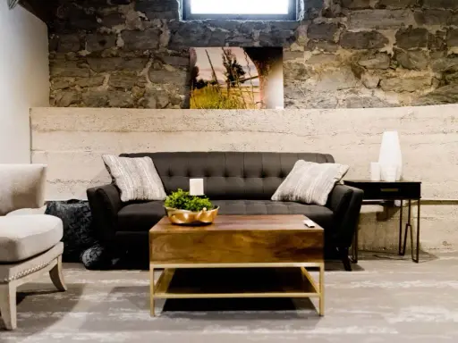Gemütliches Wohnzimmer im industrial style mit dunklem Sofa, Holztisch und Steinwand.