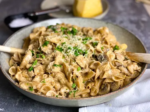 En krämig kyckling svamp pasta i en skål, toppad med persilja och parmesan.