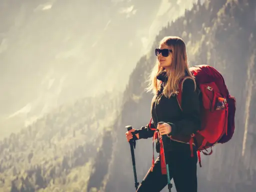 Kobieta w stroju w góry damski, z plecakiem i kijkami trekkingowymi, podziwia górski krajobraz.