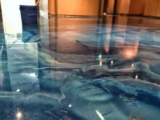 Glänzender Epoxidharzboden in Blau- und Brauntönen, der an eine Wasserlandschaft erinnert. Die Nachteile von Epoxidharz, wie die Empfindlichkeit gegenüber UV-Licht, sind hier nicht sichtbar.