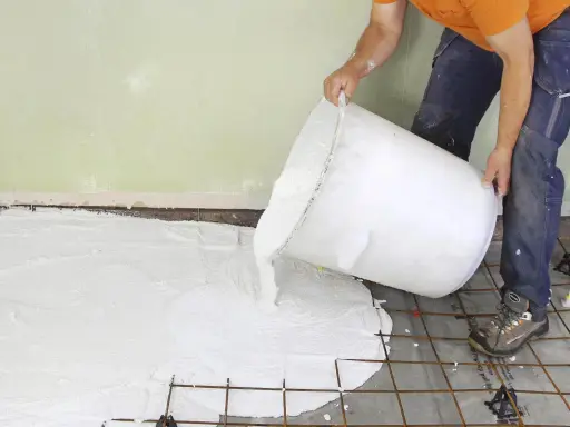 En person häller ut ett vitt material ur en stor hink över ett armeringsnät. Inspiration för betonggolv.