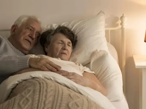Un uomo anziano abbraccia dolcemente la moglie a letto. La sua mano sulla sua pancia, forse un gesto per confortarla, perché un malato di Alzheimer dorme sempre, cercando riposo.