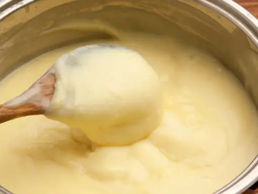 Une cuillère en bois remue une crème pâtissière maison onctueuse dans une casserole.