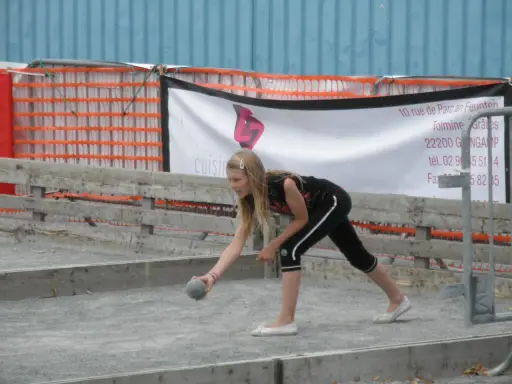 Jeune fille lançant une boule sur un terrain de pétanque, peut-être pour une partie de boule bretonne.