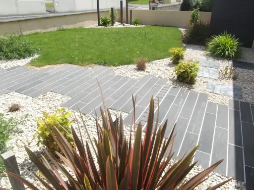 Chemin en dalles grises et gravier blanc, pelouse verte et plantes décoratives. Un jardin facile d'entretien.