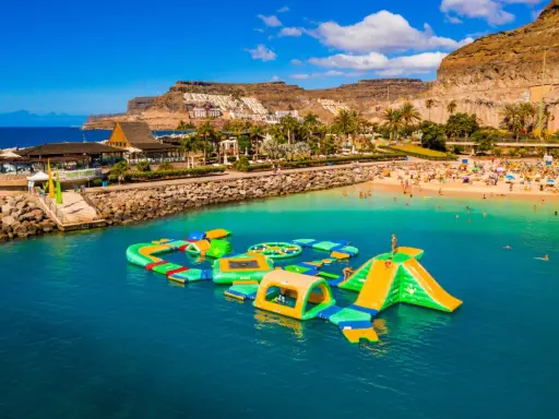 Divertimento acquatico a Gran Canaria con bambini: scivoli gonfiabili e giochi in mare su una spiaggia affollata.