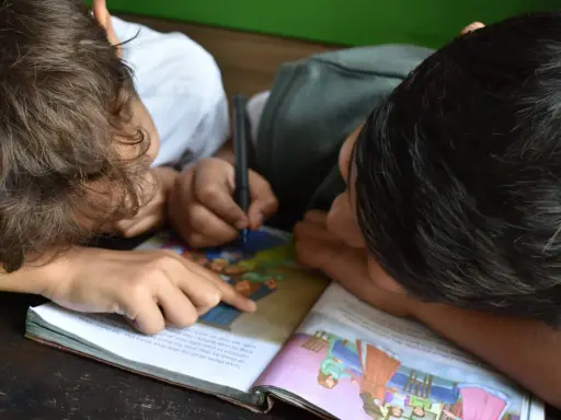 Due bambini studiano insieme, uno scrive mentre l'altro indica il libro. Un esempio di peer learning.