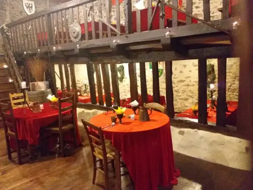 Ambiance d'une auberge moyen âge avec tables dressées de nappes rouges, poutres apparentes et murs en pierre.