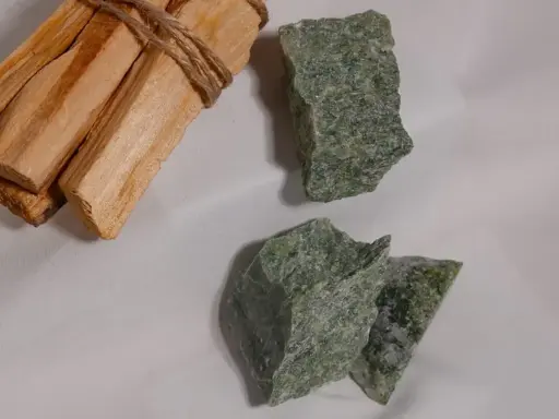 Surowe kawałki zielonego jadeitu, znanego z właściwości uspokajających, leżą obok wiązki drewna Palo Santo.
