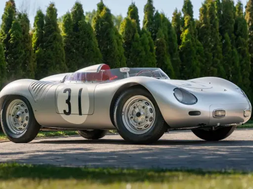 Silberner Porsche 718 RSK mit Startnummer 31, bereit für die Rennstrecke, vor einer Reihe von grünen Bäumen.