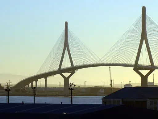 El imponente puente de Cádiz se alza sobre el agua, con sus cables tensos y pilares icónicos contra un cielo despejado.