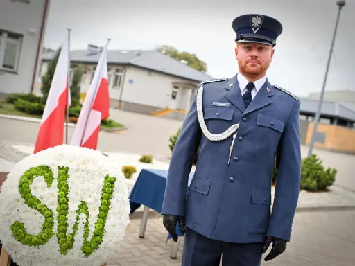 Mężczyzna w mundurze galowym SW, biało-zielony wieniec z napisem SW, polskie flagi.