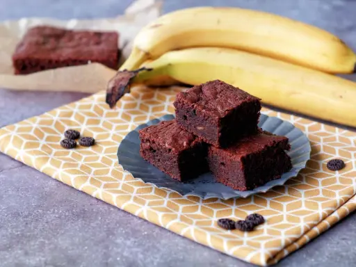 Saftige bananen brownies auf einem gelben Tuch, daneben reife Bananen.