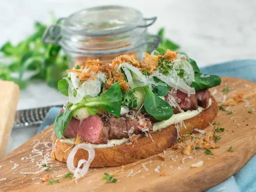 En läcker steak sandwich med saftigt kött, krispig sallad, lök och riven ost på rostat bröd.