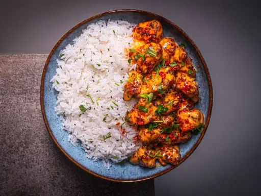 Schüssel mit weißem Reis und würzigem Bang Bang Chicken, garniert mit Koriander und Sesam.