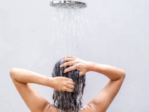 Frau wäscht sich die Haare unter der Dusche, eine natürliche Methode, um die Haare ohne Shampoo zu reinigen.