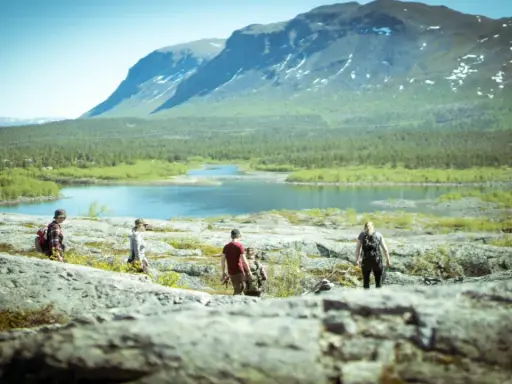 Vandring i **Laponia nationalpark** med fjäll, sjö och skog. En grupp vandrare njuter av den storslagna naturen.