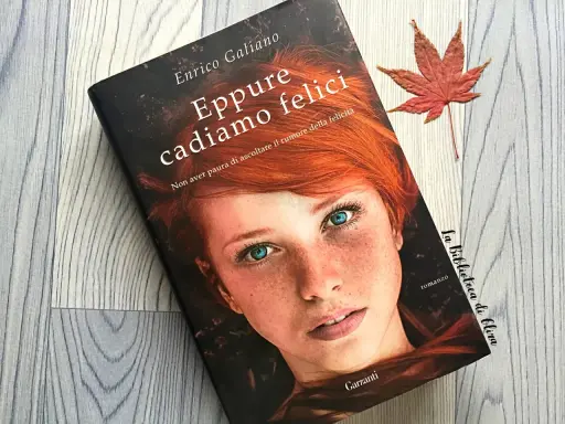 Copertina del libro "Eppure cadiamo felici" di Enrico Galiano, con il volto di una ragazza dai capelli rossi e occhi azzurri. Una foglia d'acero rossa completa la scena.