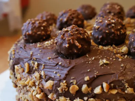 Pyszny tort ferrero rocher, obficie udekorowany czekoladowymi kulkami i posypany orzechami.
