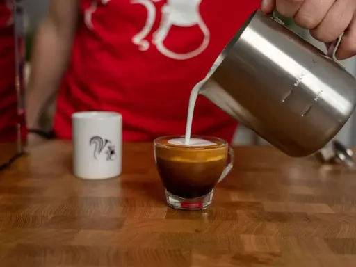 Milchschaum fließt in einen Espresso, um einen perfekten Espresso Macchiato zu kreieren.