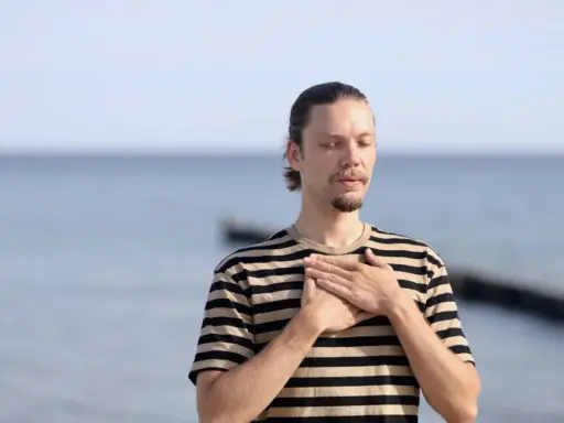 Mann mit geschlossenen Augen und Händen auf der Brust, genießt die frische Meeresluft. Eine asthma kur am meer kann Wunder wirken.