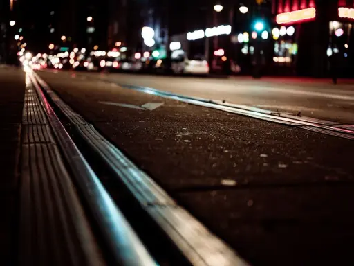 Torowisko tramwajowe w nocy, światła miasta rozmyte, jakby w ślepocie zmierzchowej.