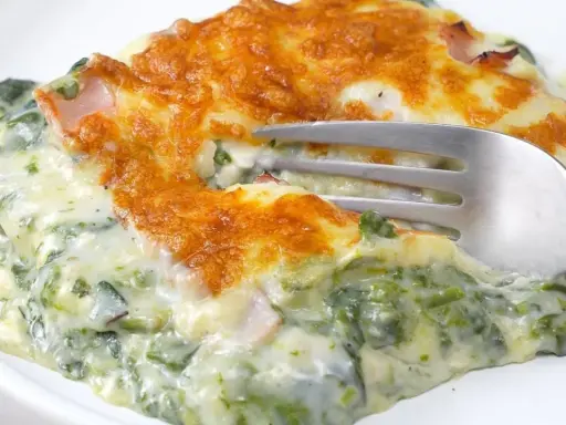 Deliciosa lasaña de espinacas cremosa, gratinada y lista para disfrutar. Un tenedor se hunde en esta maravilla.