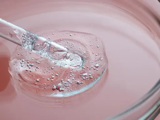 Goccia di siero trasparente con bollicine, su sfondo rosa. Un tocco di vitamina B3 per il viso.