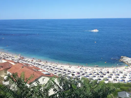 Le spiagge di Numana, con ombrelloni colorati e gente che si gode il sole, bagnate da un mare azzurro e calmo. Una barca solca l'orizzonte.