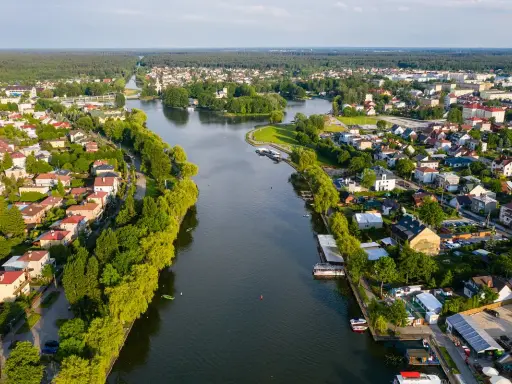 Malowniczy widok na Augustów i jego atrakcje: rzeka, zielone brzegi, domy i las w tle.