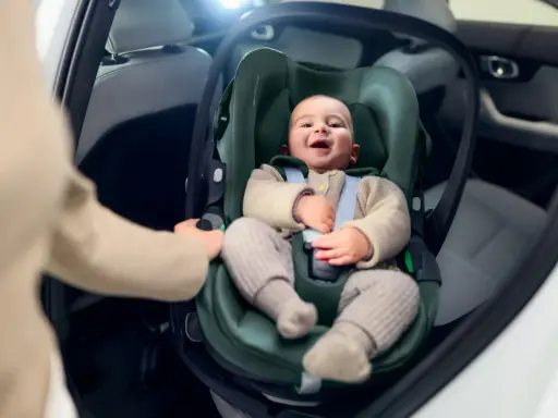 Uśmiechnięte dziecko w foteliku samochodowym. Ręka rodzica pokazuje, jak wypiąć fotelik z bazy isofix.