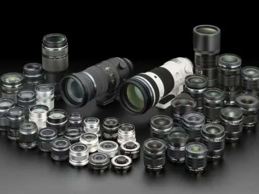 Collezione di obiettivi fotografici di varie dimensioni, dai teleobiettivi ai grandangolari, disposti su sfondo nero. Un vero tesoro per ogni appassionato di termini fotografici.