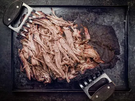 Zartes pulled beef, frisch aus dem Dutch Oven, wird mit Fleischkrallen zerteilt. Perfekt für BBQ!