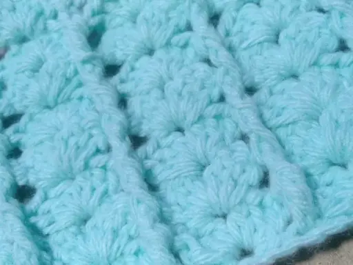 Textura de un tejido a crochet en tono azul claro. Se aprecian los detalles de un punto fantasía, creando un patrón con relieve y pequeños huecos.
