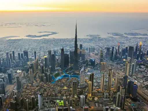 Luftaufnahme von Dubai bei Sonnenuntergang. Der Burj Khalifa ragt empor, umgeben von Wolkenkratzern und den künstlichen Inseln. Ein Blick auf die Dubai Besonderheiten.