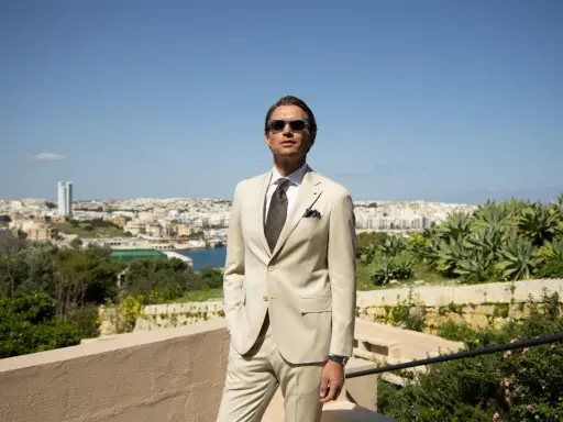 A man in a light tan suit, tie, and sunglasses offers inspiration for what to wear to a communion as a guest male.