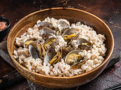 Un delicioso arroz con almejas, servido en un cuenco de madera. Las almejas, abiertas y jugosas, se mezclan con el arroz cremoso.