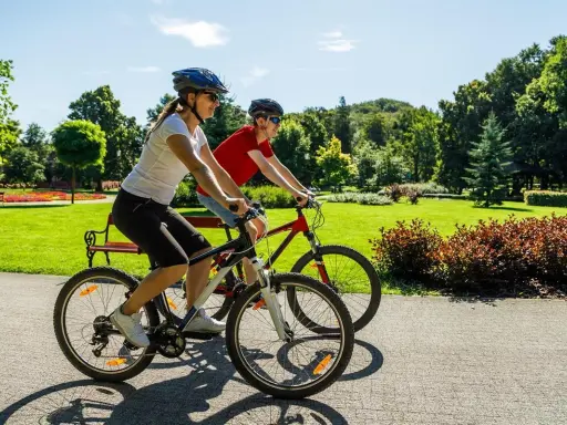 Dwie osoby na rowerach cieszą się piękną pogodą w parku. To pokazuje, co daje jazda na rowerze: aktywność, relaks i kontakt z naturą.