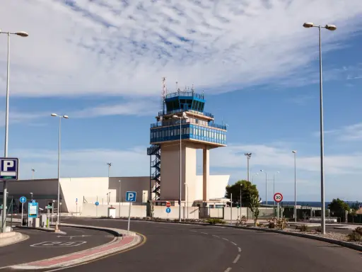 Kontrollturm am Almeria Airport mit Parkplatzschildern und Straßenbeleuchtung unter blauem Himmel.