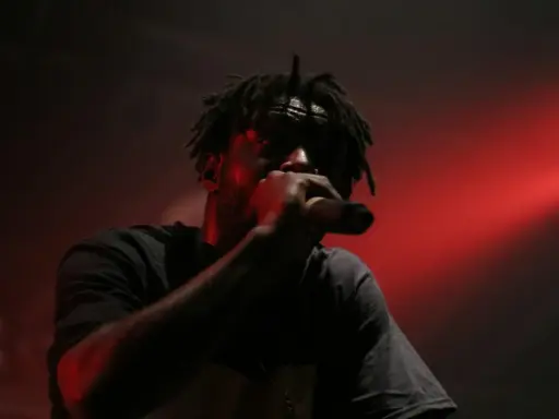 En 90 tals rappare med dreadlocks framför en röd ljusshow, svettig och fokuserad på mikrofonen.
