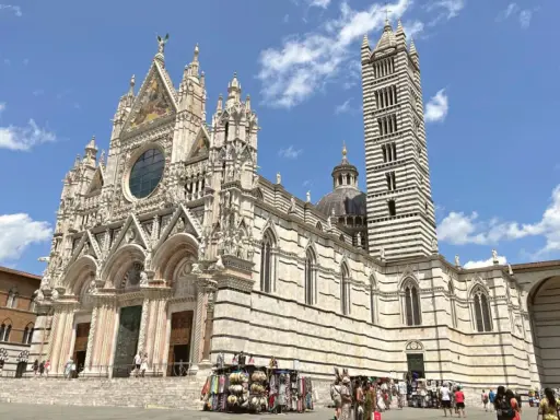 Il Duomo di Siena, con la sua imponente torre campanaria a strisce, è un must per chi cerca cosa visitare a Siena. La piazza antistante è animata da bancarelle.