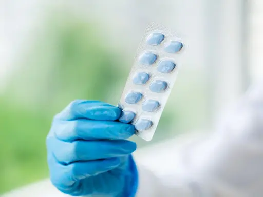 Ręka w niebieskiej rękawiczce trzyma opakowanie niebieskich tabletek. To może być alternatywa dla naturalnych suplementów na potencję.