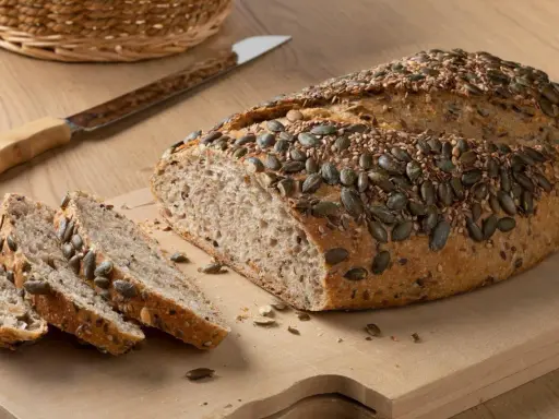 Chleb z mąki orkiszowej, posypany pestkami dyni i sezamem, pokrojony na desce.