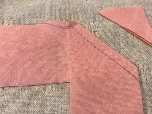 Rosa tygbitar sys ihop med snedslå. En liten triangel ligger bredvid.