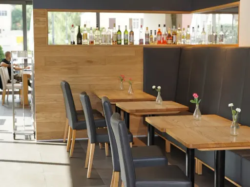 Mesas de madera con floreros y sillas negras en un restaurante. La distancia entre mesas permite un espacio cómodo.