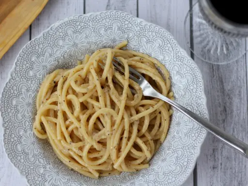 Porcja pysznego cacio e pepe na ozdobnym talerzu, z widelcem w makaronie.